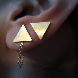 May include: A pair of gold triangle earrings with a chain dangling from one earring.