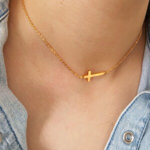May include: A gold chain necklace with a small, sideways cross pendant.