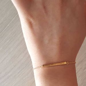 May include: A gold chain bracelet with a thin, horizontal bar charm.