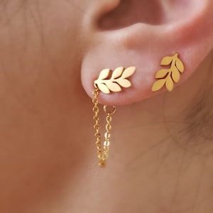 以下が含まれることがあります： 金色の葉っぱの形をしたイヤリングに、チェーンがぶら下がっています。イヤリングは葉っぱの枝の形をしています。