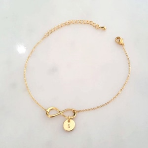 May include: Gold infinity charm bracelet with a small round charm engraved with the letter "S".