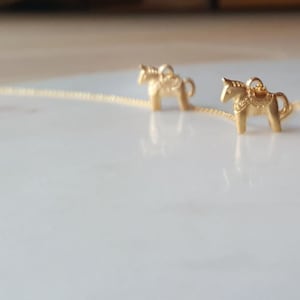 May include: Three gold-colored Dala horse charms on a delicate chain necklace. The charms are detailed with traditional Swedish Dala horse designs.