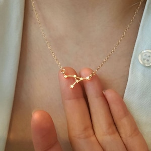 May include: A gold necklace featuring a dainty constellation pendant. The pendant is shaped like the Cancer constellation, with small sparkling stones representing the stars.