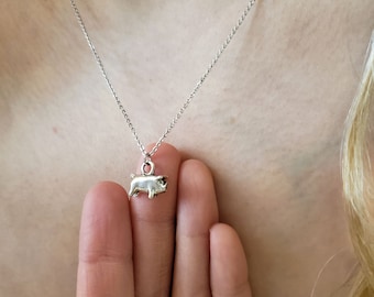 May include: A silver necklace with a small pig charm. The pig is facing to the right and has a slightly curled tail.
