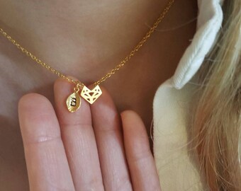 Puede incluir: Un collar de cadena dorada con un pequeño colgante geométrico y un dije con la letra "E" colgando.