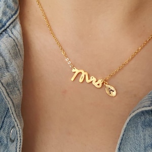 Puede incluir: Collar de oro con un colgante de "Mrs." en cursiva y un pequeño dije con la letra "A" colgando.