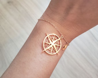 May include: A gold compass charm bracelet with a delicate chain. The compass charm has a detailed design with a star in the center.