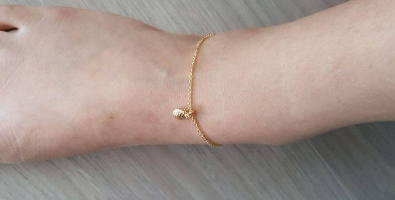 K&ouml;nnte beinhalten: Ein goldenes Fu&szlig;kettchen mit einem kleinen Ananas-Anh&auml;nger.