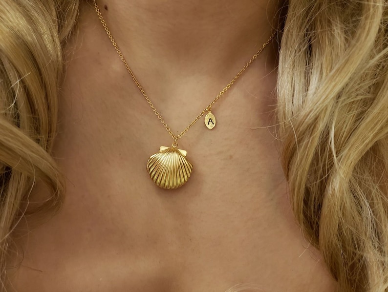 May include: A gold necklace with a seashell pendant and a small letter 'A' charm.