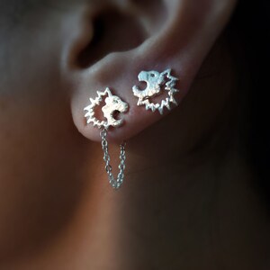 May include: A pair of silver earrings with a chain connecting them. Each earring features a detailed design of a lion's head.