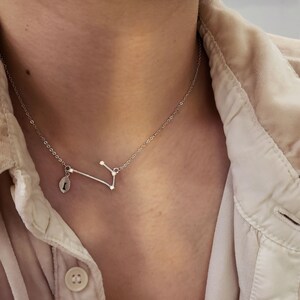 May include: A silver necklace with a constellation pendant and a small charm. The pendant is a delicate design of a constellation with small stars.