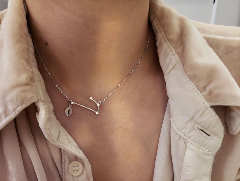 May include: A silver necklace with a constellation pendant and a small charm. The pendant is a delicate design of a constellation with small stars.