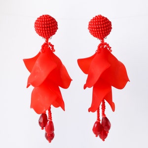 May include: A pair of red dangle earrings with a beaded top and multiple layers of red fabric petals. The earrings have a dangling red bead at the bottom.