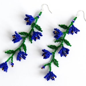 May include: A pair of blue and green beaded earrings shaped like flower blossoms. The earrings are made with small, round beads and have a delicate, feminine design.