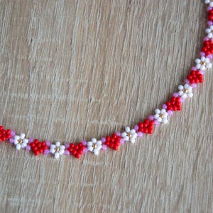 Peut inclure: Un collier de perles avec un motif r&eacute;p&eacute;titif de fleurs rouges, blanches et roses.