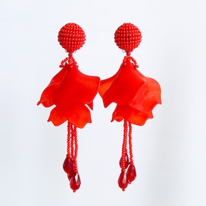 以下が含まれることがあります： 赤いビーズのドロップイヤリング。赤い花の形をしたチャームと赤いクリスタルがぶら下がっています。