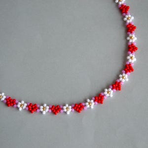 Peut inclure: Un collier d&eacute;licat en perles avec un motif r&eacute;p&eacute;titif de fleurs rouges, blanches et roses.