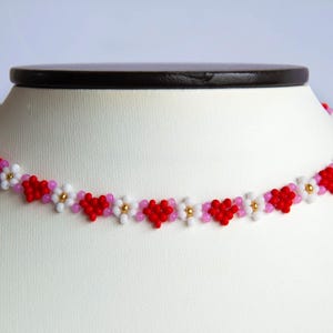 Peut inclure: Un collier ras de cou en perles rouges, roses et blanches avec un motif floral.