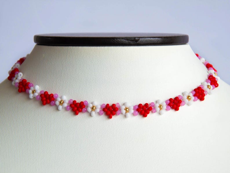 Peut inclure: Un collier ras de cou en perles rouges, roses et blanches avec un motif floral.