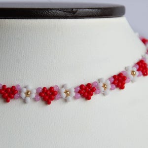 Peut inclure: Un collier ras de cou en perles rouges, blanches et roses avec un motif en forme de c&oelig;ur. Le collier est fait de petites perles et a un aspect d&eacute;licat.