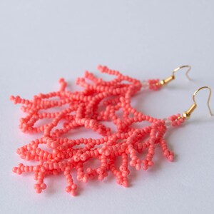 May include: Coral pink beaded earrings with gold hooks. The earrings are made of small beads that are strung together to create a fringe effect.