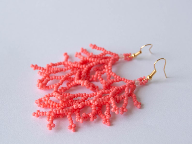 May include: Coral pink beaded earrings with gold hooks. The earrings are made of small beads that are strung together to create a fringe effect.