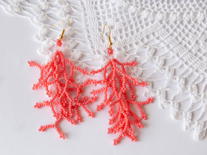 May include: A pair of coral-coloured beaded earrings shaped like coral branches. The earrings are hanging from gold hooks.