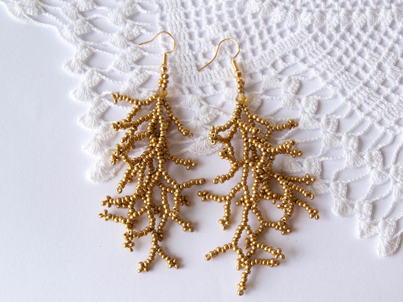 May include: A pair of gold beaded earrings with a delicate, branch-like design. The earrings are long and dangle, with a gold hook fastening.