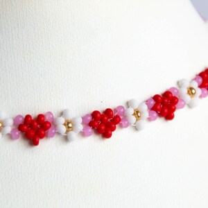 Peut inclure: Un collier d&eacute;licat compos&eacute; de petites perles rouges, blanches et roses dispos&eacute;es en forme de fleurs.