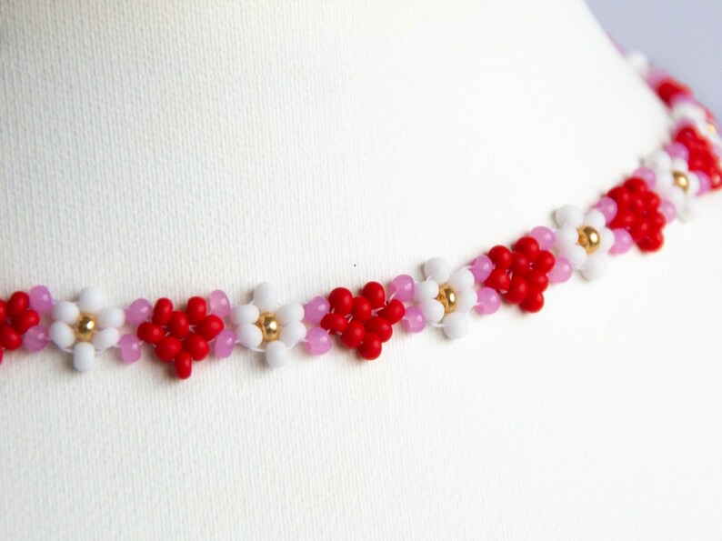 Peut inclure: Un collier d&eacute;licat compos&eacute; de petites perles rouges, blanches et roses dispos&eacute;es en forme de fleurs.