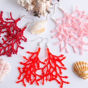 Puede incluir: Tres pares de pendientes de coral con cuentas en rojo, rosa y naranja. Los pendientes tienen forma de ramas de coral y cuelgan de ganchos plateados.