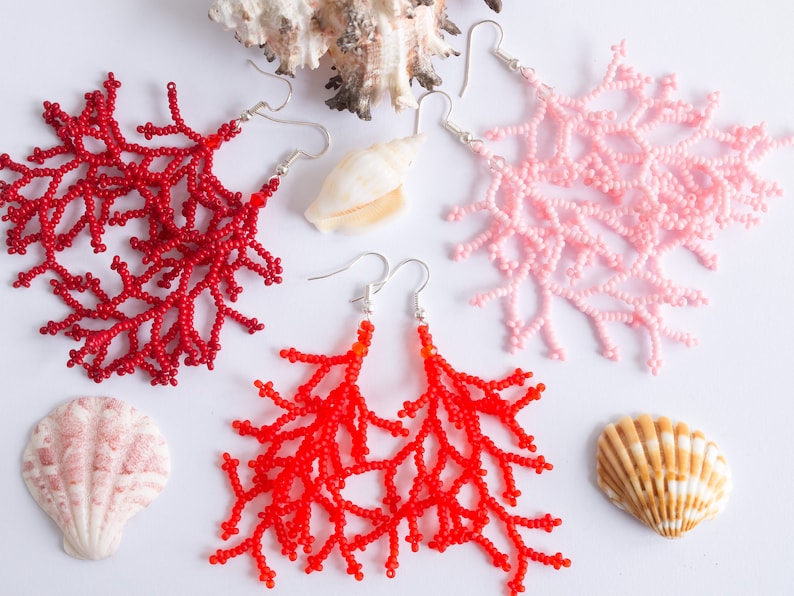 Puede incluir: Tres pares de pendientes de coral con cuentas en rojo, rosa y naranja. Los pendientes tienen forma de ramas de coral y cuelgan de ganchos plateados.