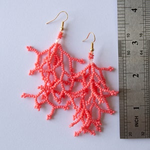 May include: Coral-coloured beaded earrings shaped like coral branches, hanging from gold hooks. The earrings are approximately 5 cm long.