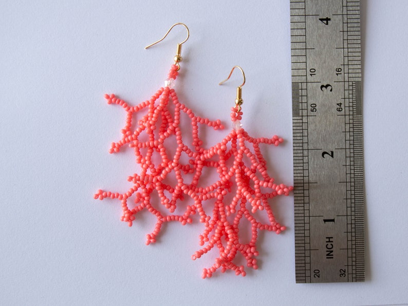 May include: Coral-coloured beaded earrings shaped like coral branches, hanging from gold hooks. The earrings are approximately 5 cm long.