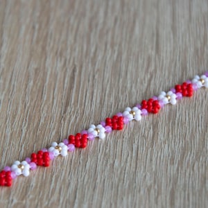 Peut inclure: Un bracelet en perles avec un motif r&eacute;p&eacute;t&eacute; de perles rouges, blanches et roses. Les perles sont dispos&eacute;es en forme de fleur.