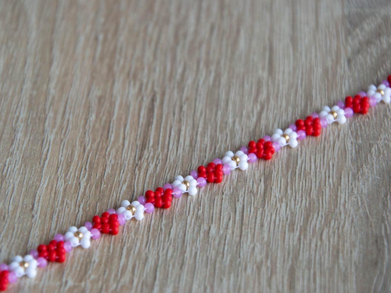 Peut inclure: Un bracelet en perles avec un motif r&eacute;p&eacute;t&eacute; de perles rouges, blanches et roses. Les perles sont dispos&eacute;es en forme de fleur.