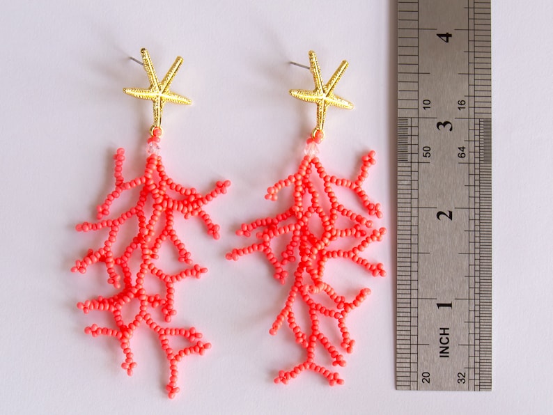 Puede incluir: Un par de pendientes de cuentas de color coral con abalorios de estrella de mar dorados. Los pendientes miden aproximadamente 5 cm de largo.