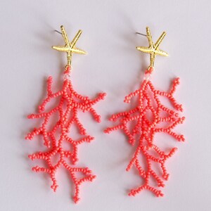 Puede incluir: Un par de pendientes de cuentas de color coral con abalorios de estrella de mar dorados. Los pendientes son largos y colgantes, con las cuentas de coral formando un delicado dise&ntilde;o de ramas.