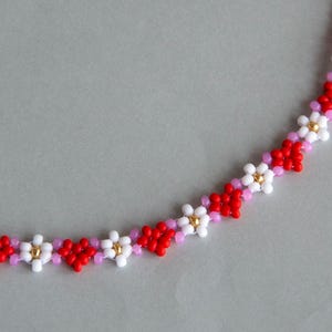 Peut inclure: Un collier de perles avec un motif r&eacute;p&eacute;titif de fleurs rouges, blanches et roses.