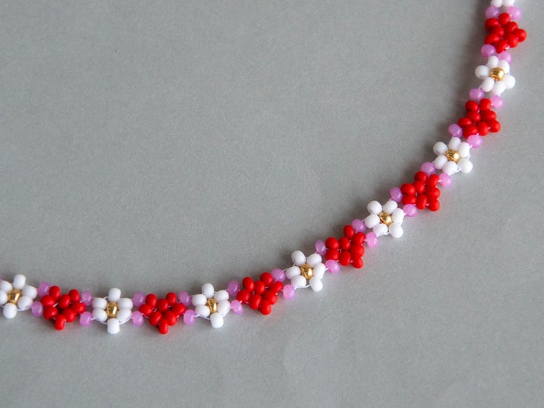 Peut inclure: Un collier de perles avec un motif r&eacute;p&eacute;titif de fleurs rouges, blanches et roses.