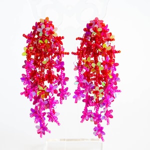 May include: A pair of dangle earrings featuring a gradient of red and pink sequins in the shape of flowers.