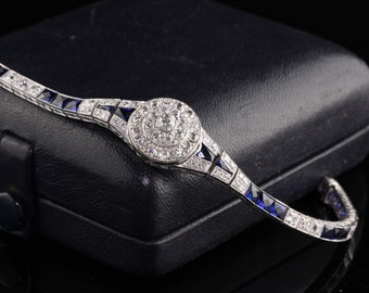 Peut inclure: Un bracelet en argent avec un centre rond en cristal clair entouré de petits cristaux. Le bracelet est serti de pierres bleues carrées.