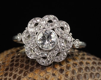 Könnte beinhalten: Ein silberner Ring mit einem großen, runden, klaren Diamanten, der von kleineren Diamanten in einem floralen Design umgeben ist.
