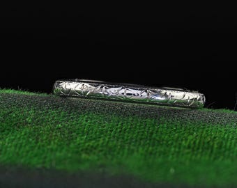 Puede incluir: Una alianza de plata con un diseño delicado e intrincado. La banda está sobre una superficie verde.