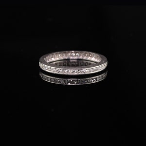 May include: A silver band ring with a row of small diamonds set in a channel setting.