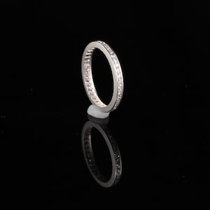 May include: A silver band ring with a row of small, clear diamonds set into the band.