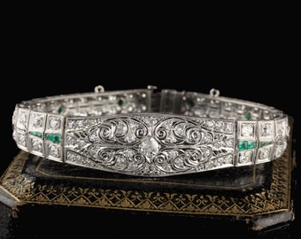 May include: A delicate diamond and emerald bracelet with an intricate floral design. The bracelet is set in platinum and features a central round diamond surrounded by smaller diamonds and emerald accents.