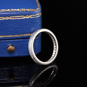 May include: A thin silver band with small diamonds set in a channel setting. The band is inscribed with the letters "E.M.S.T."