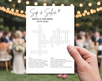 May include: A white card with a crossword puzzle titled "Sip & Solve" for Michelle and Mark, dated 09.01.2025. The puzzle includes clues about their wedding, favorite things, and shared interests. The card is held in front of a blurred outdoor background.