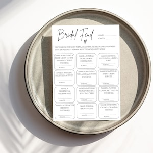 May include: A printable bridal shower game called "Bridal Feud" with a heart symbol. The game asks guests to guess the most popular answers to questions about weddings and bridal showers. The person with the most points wins.